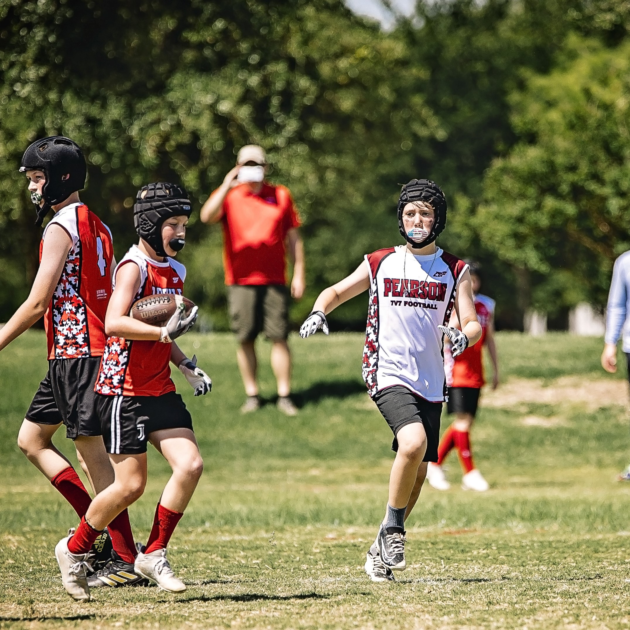 Youth players wearing protective headgear compete during a 7-on-7 football game